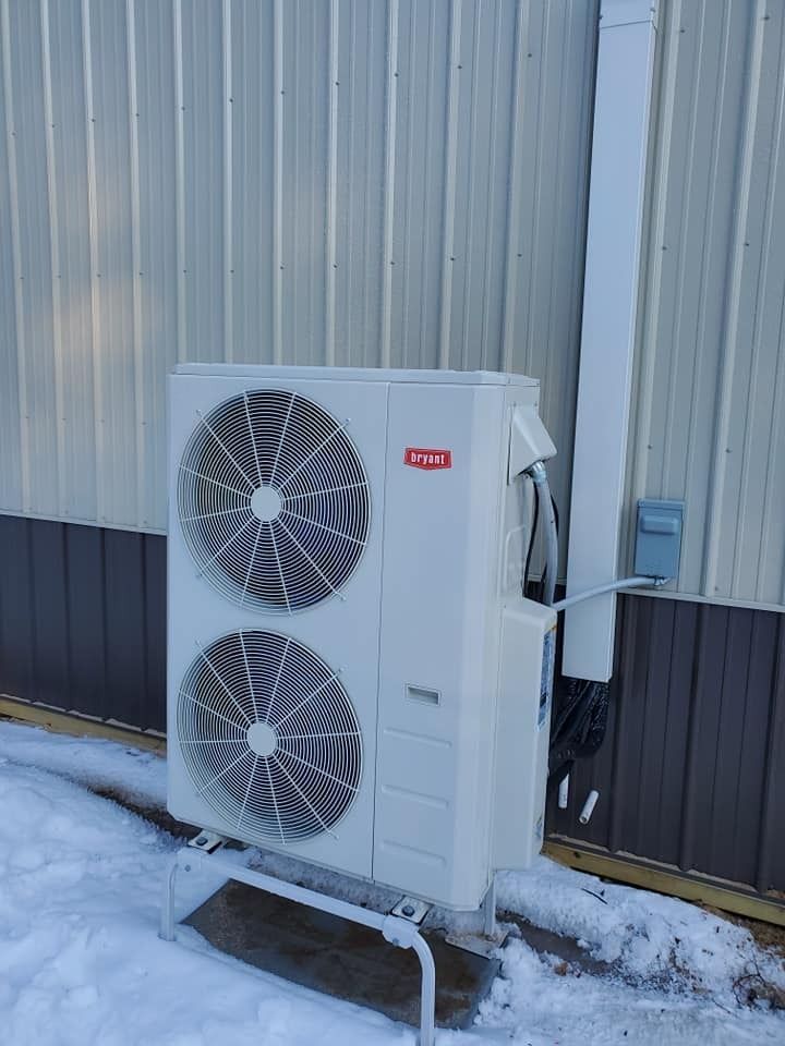 A large white air conditioner is sitting outside of a building in the snow.