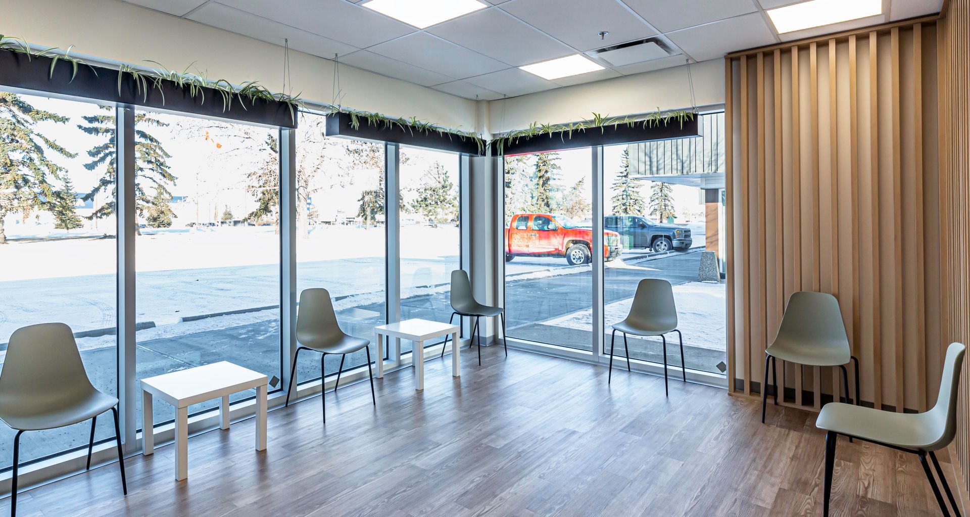 A waiting room with chairs and tables and a lot of windows.