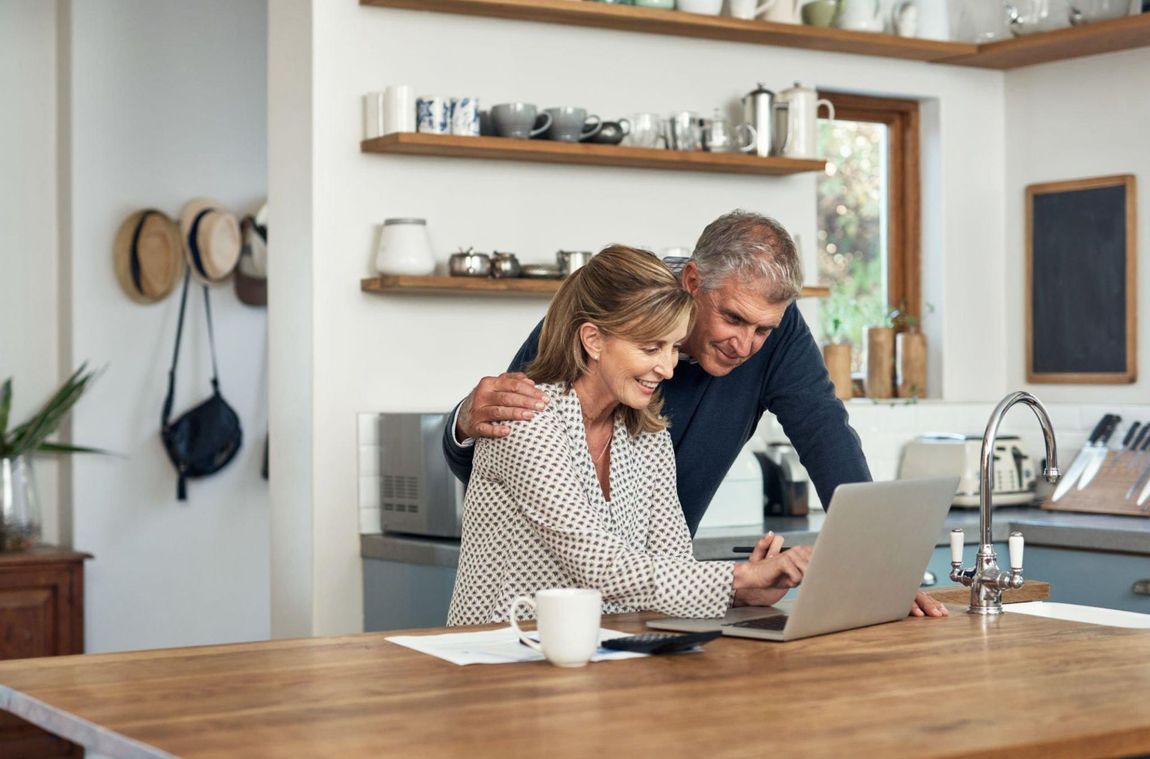 A man and woman are looking at a laptop computer in a kitchen.