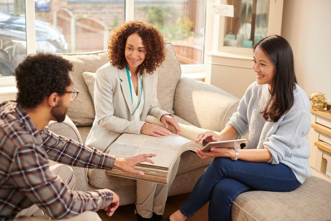 A woman is sitting on a couch talking to a man and a woman.