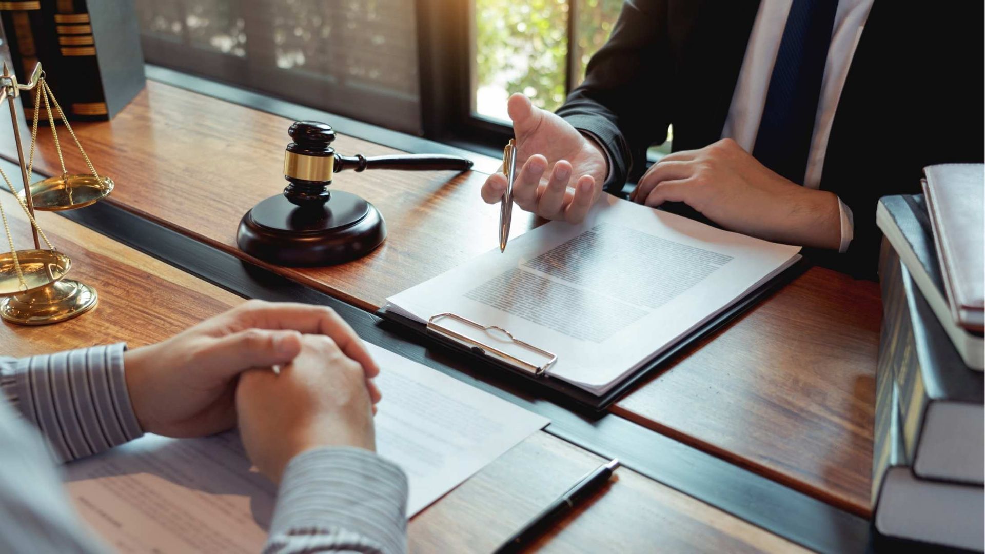 Lawyer discussing paperwork with client at a wooden desk, law books, gavel, scales of justice.