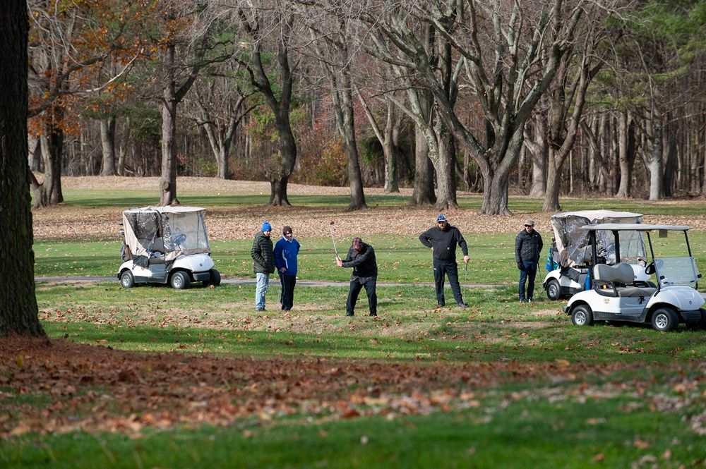 A group of people are standing next to golf carts on a golf course.