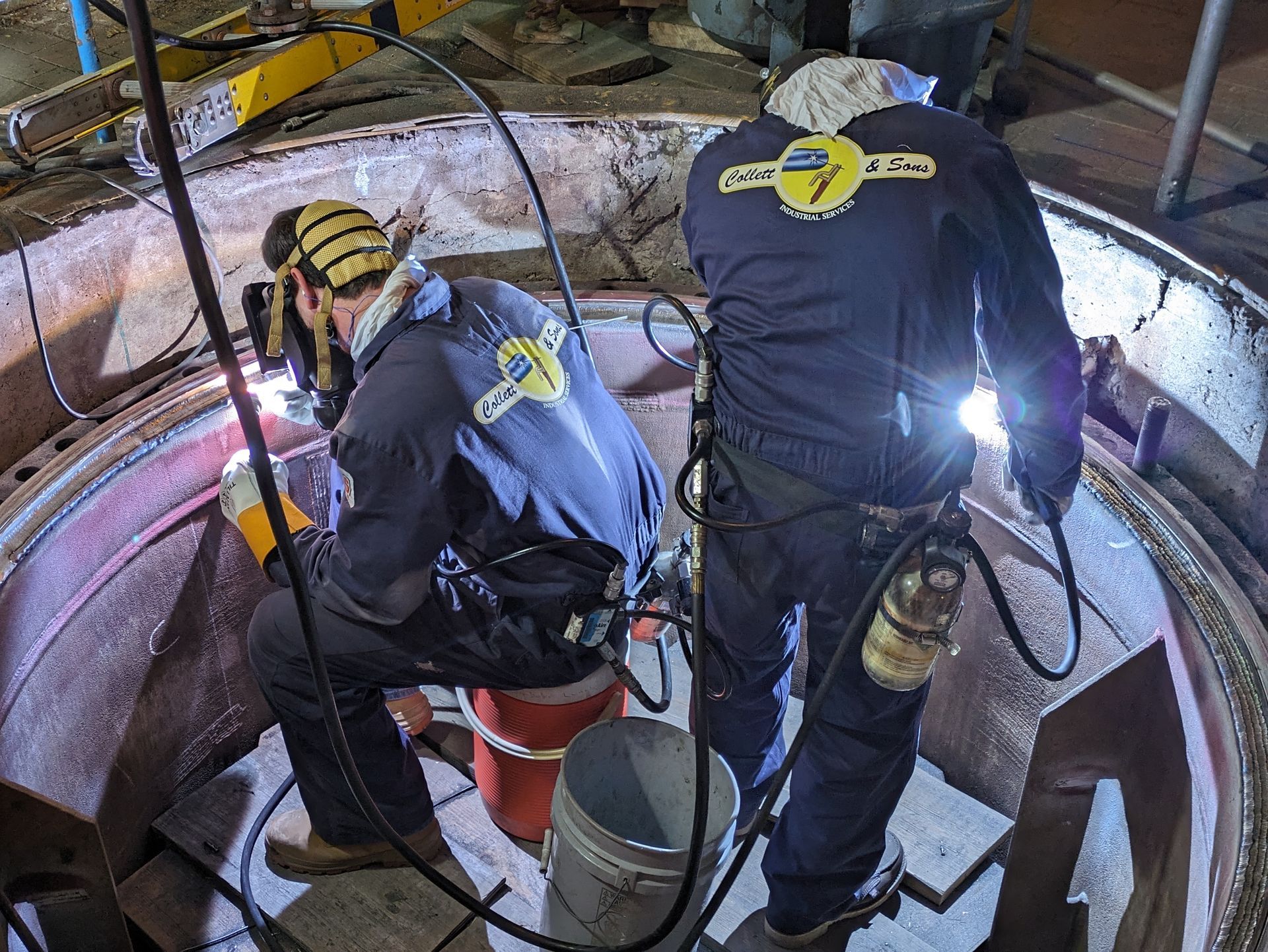 Two men are welding a piece of metal in a factory.