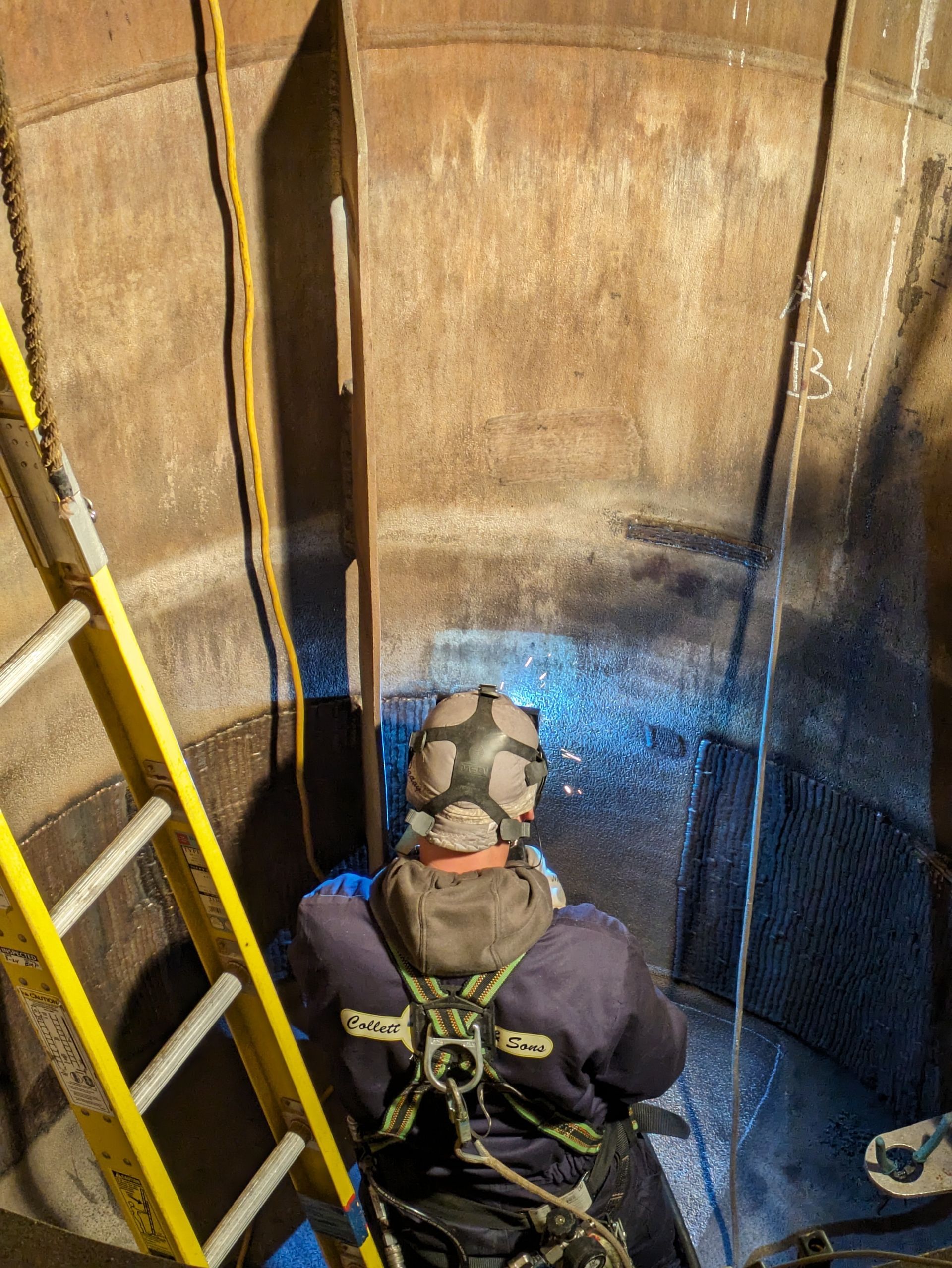 A man wearing a gas mask is sitting on a ladder in a tank.