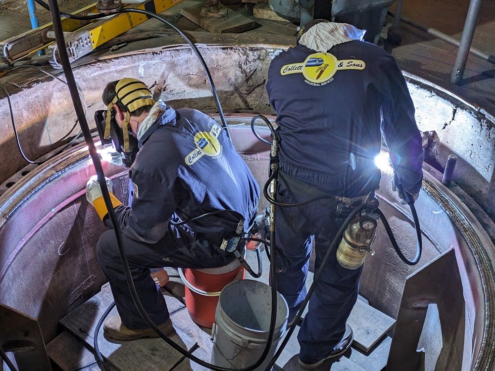 Two men are welding a piece of metal in a factory.