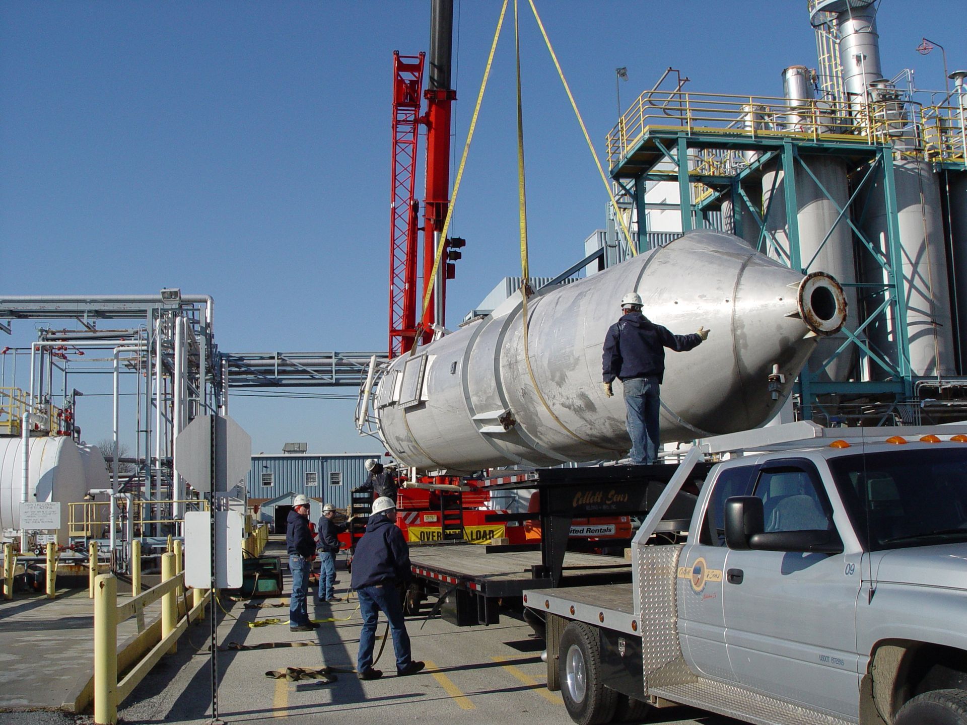 A large stainless steel cylinder is being lifted by a crane