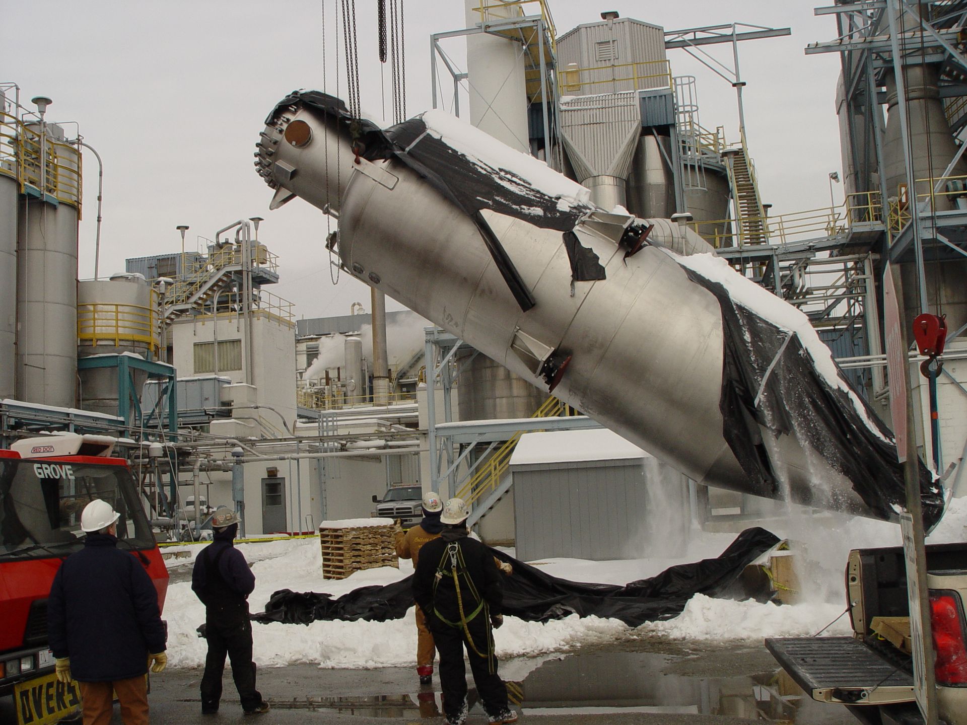 A large metal object is being lifted by a crane in a factory