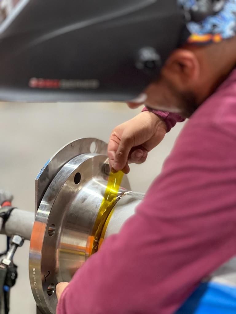 A man wearing a welding helmet is working on a piece of metal.