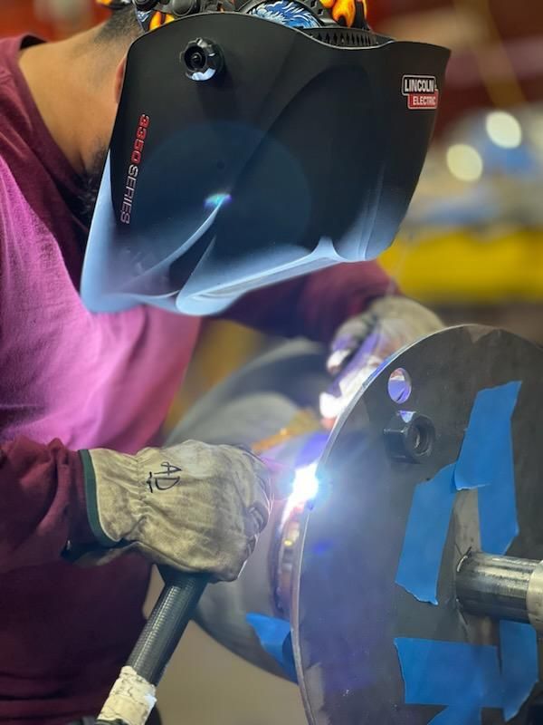 A man wearing a welding helmet is welding a piece of metal.
