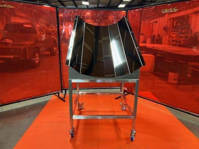 A large piece of metal is sitting on an orange mat in front of a red curtain.