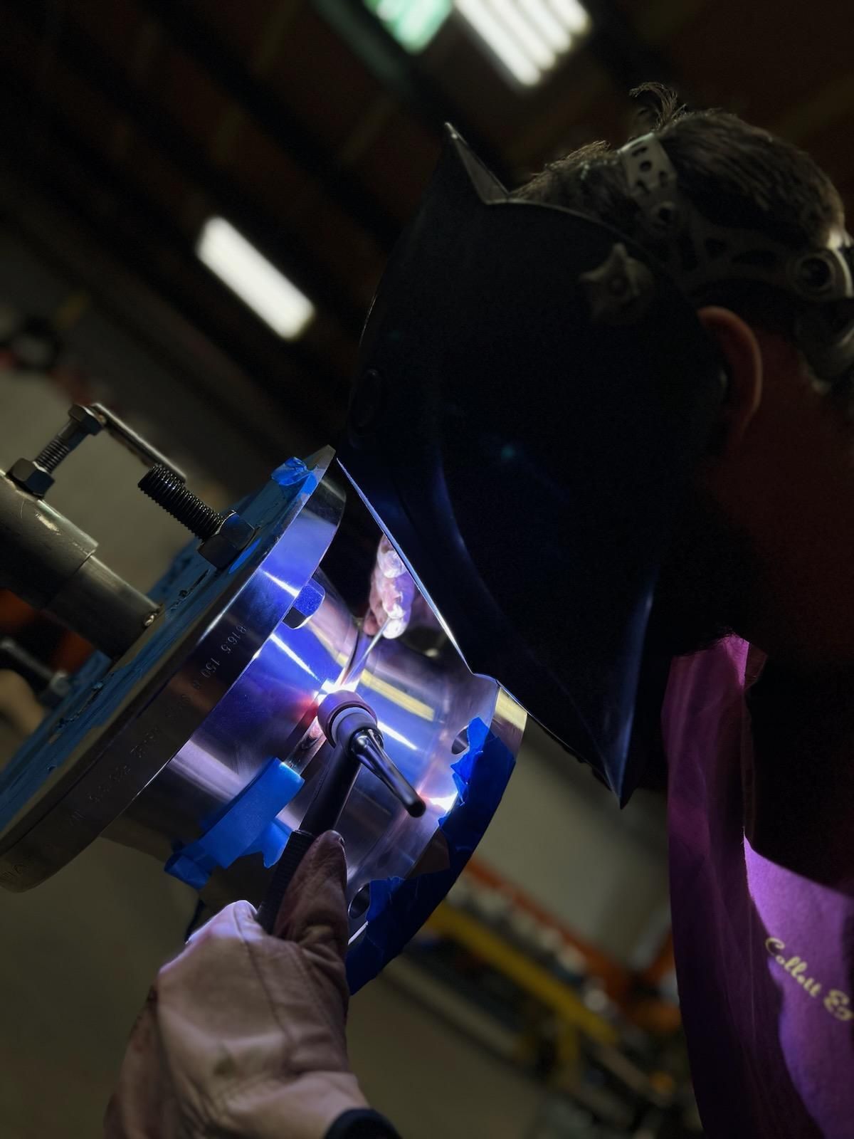 A man wearing a welding mask is working on a piece of metal