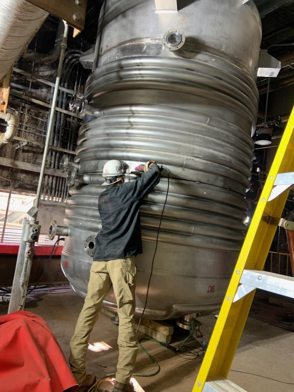 A large metal object is being lifted by a crane in a factory