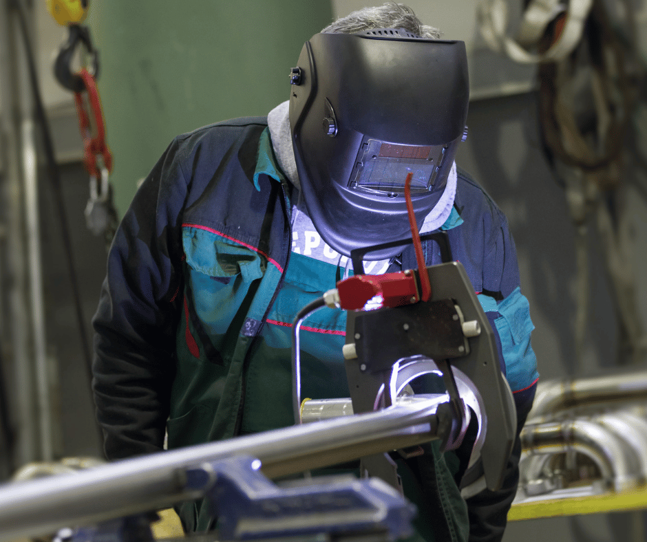 A man wearing a welding mask is working on a piece of metal.