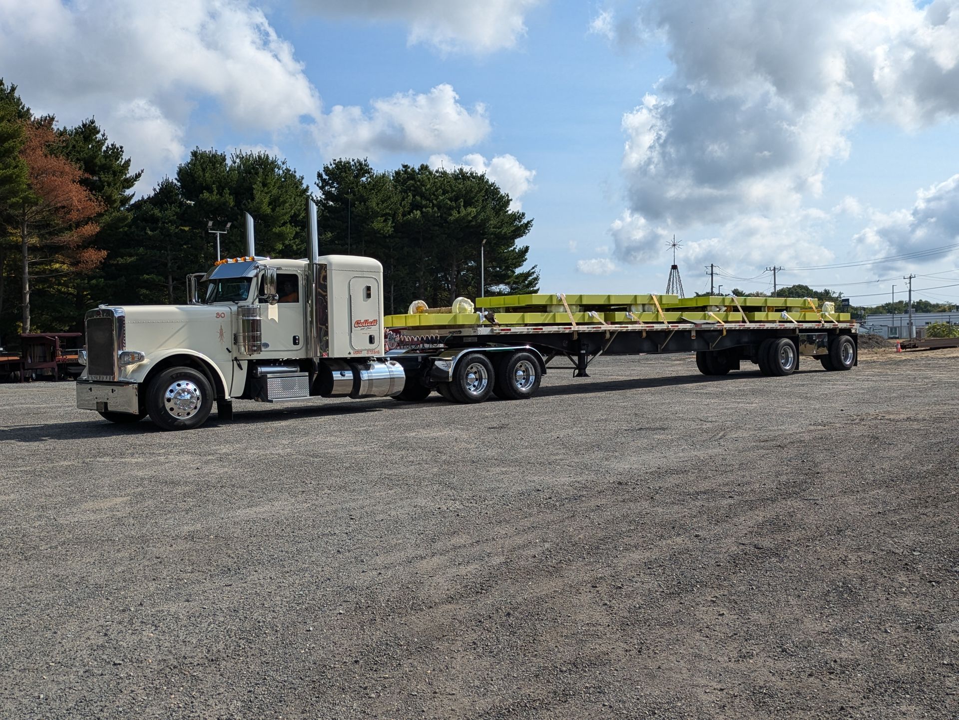 A semi truck with a flatbed trailer is parked in a gravel lot.