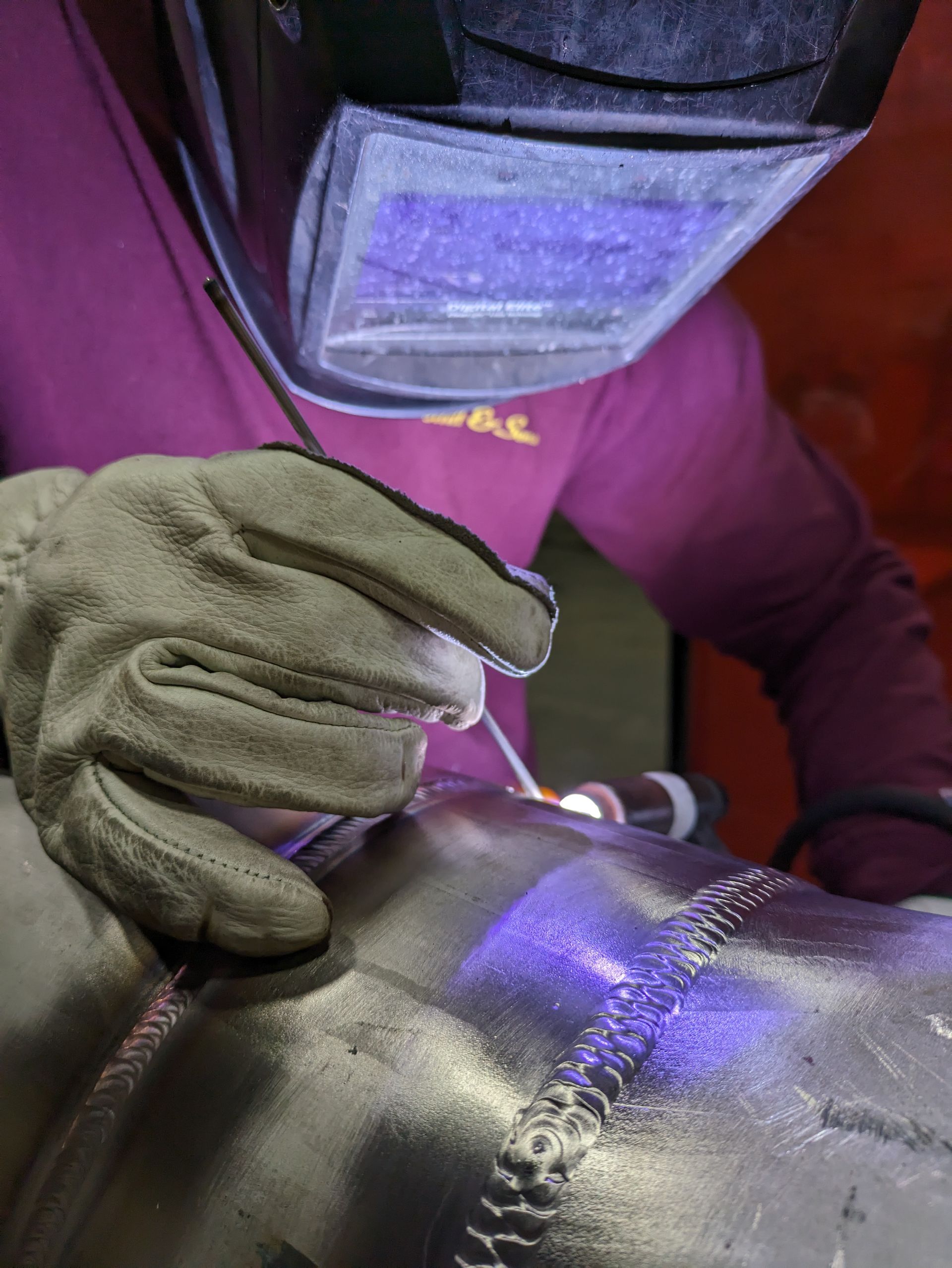 A person wearing a welding mask and gloves is welding a piece of metal.
