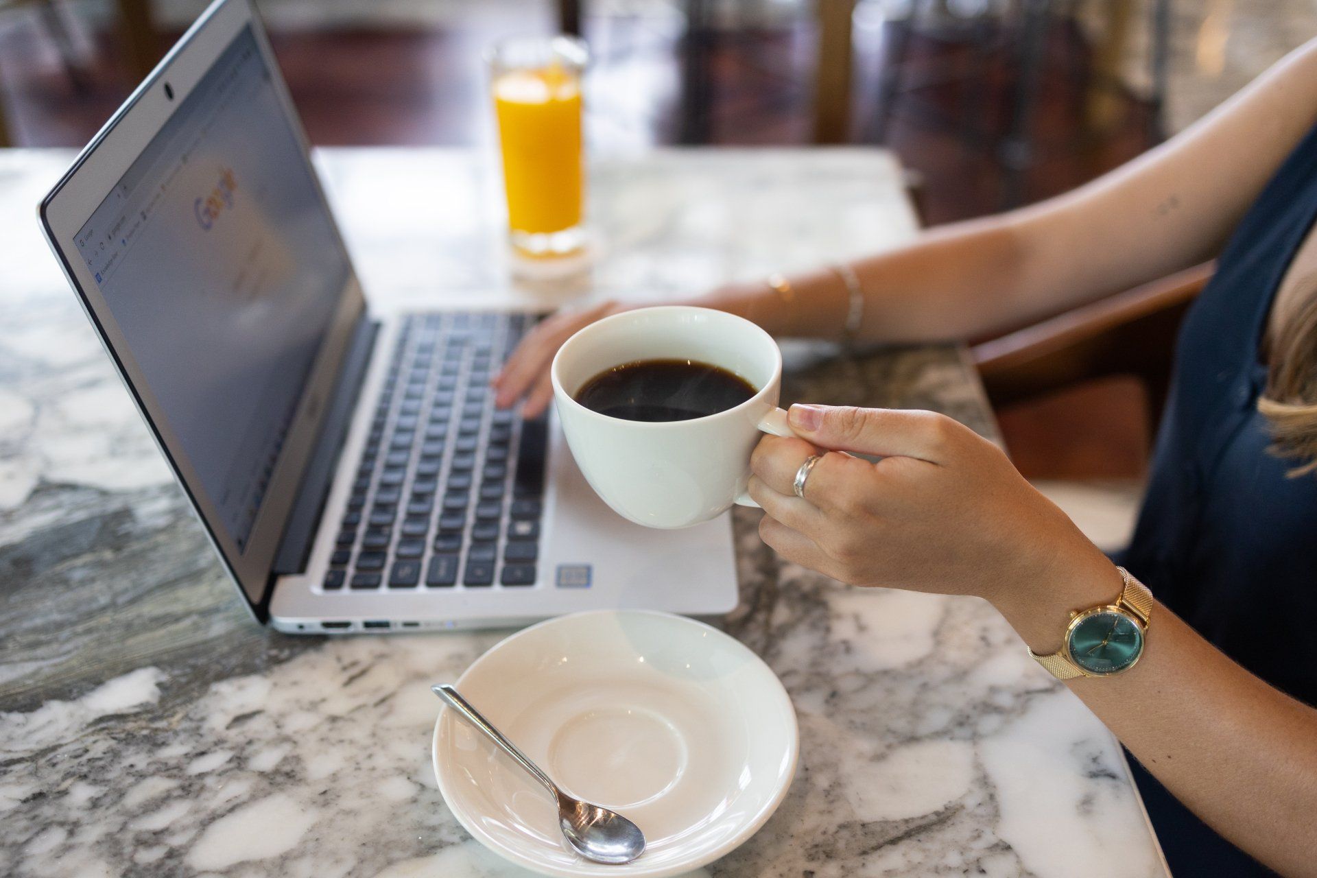 Website Design.  A woman is sitting at a table with a cup of coffee and a laptop.