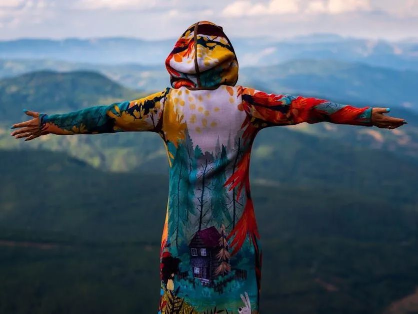 Front of the Line SEO. A person in a colorful hoodie is standing on top of a mountain with their arms outstretched.