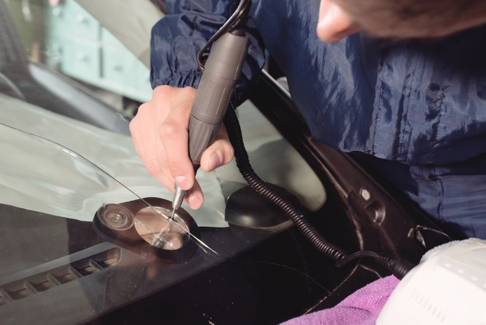 Person Repairs A Windshield, Holding Tool Near A Glass Crack.  Close-up Shot Of A Vehicle's Front