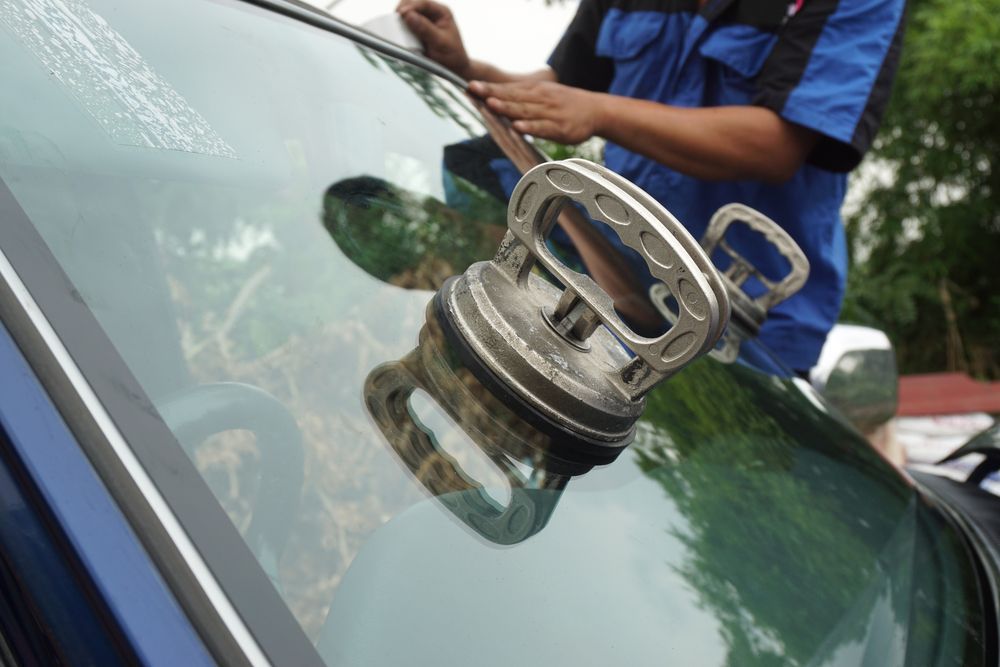 Mechanic Using A Suction Cup Tool To Remove A Windshield. The Tool Is Silver, And The Mechanic Is Wearing A Blue Uniform — Morayfield Autoglass in Caboolture South, QLD