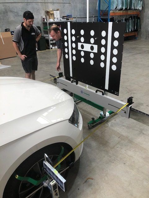 A Man is Measuring the Alignment of a White Car — Morayfield Autoglass in Caboolture South, QLD