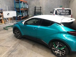 A Blue and White Car is Parked in a Garage Next to a White Van — Morayfield Autoglass in Caboolture South, QLD