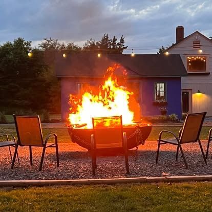 Backyard fire pit blazing at dusk with four chairs around it and a house in the background
