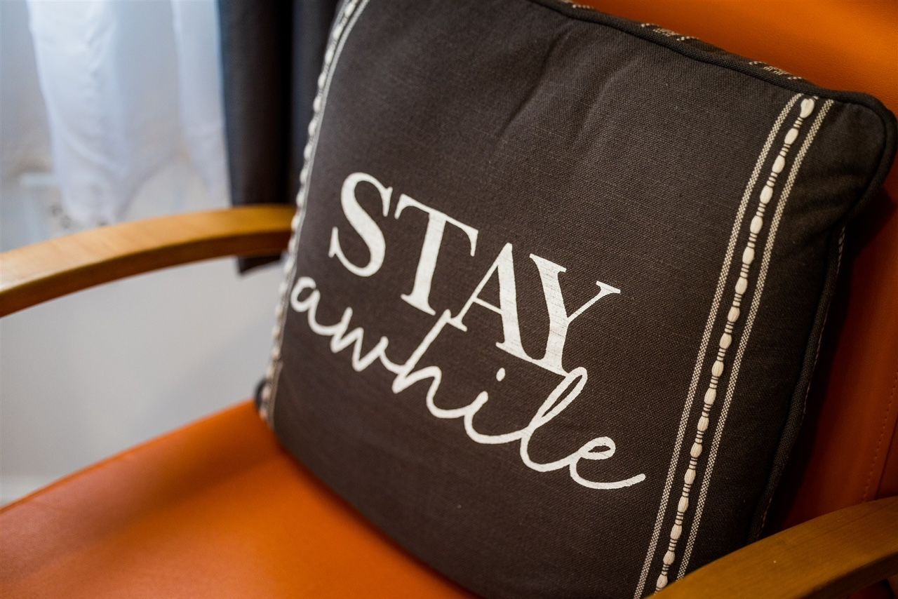 a pillow on a chair that says stay awhile