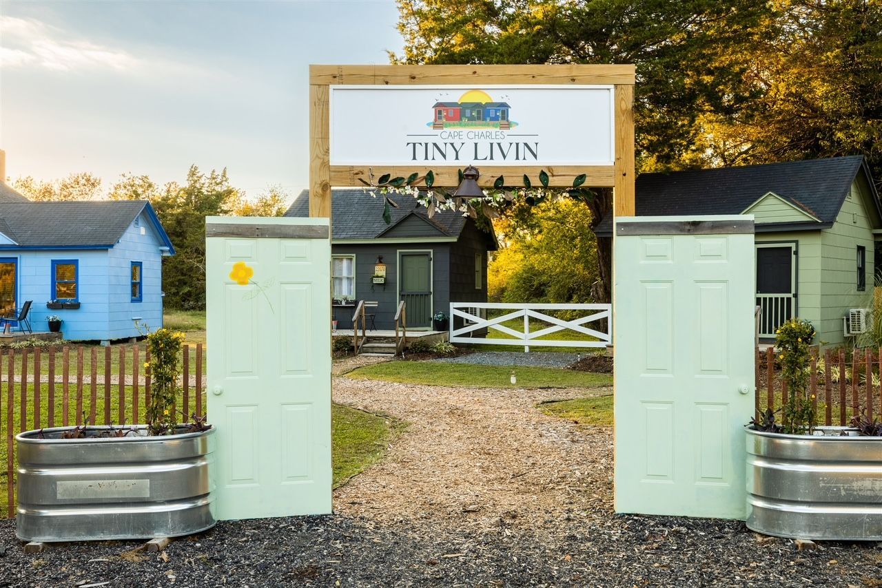 a sign that says `` tiny living '' is above a gate leading to a small house .