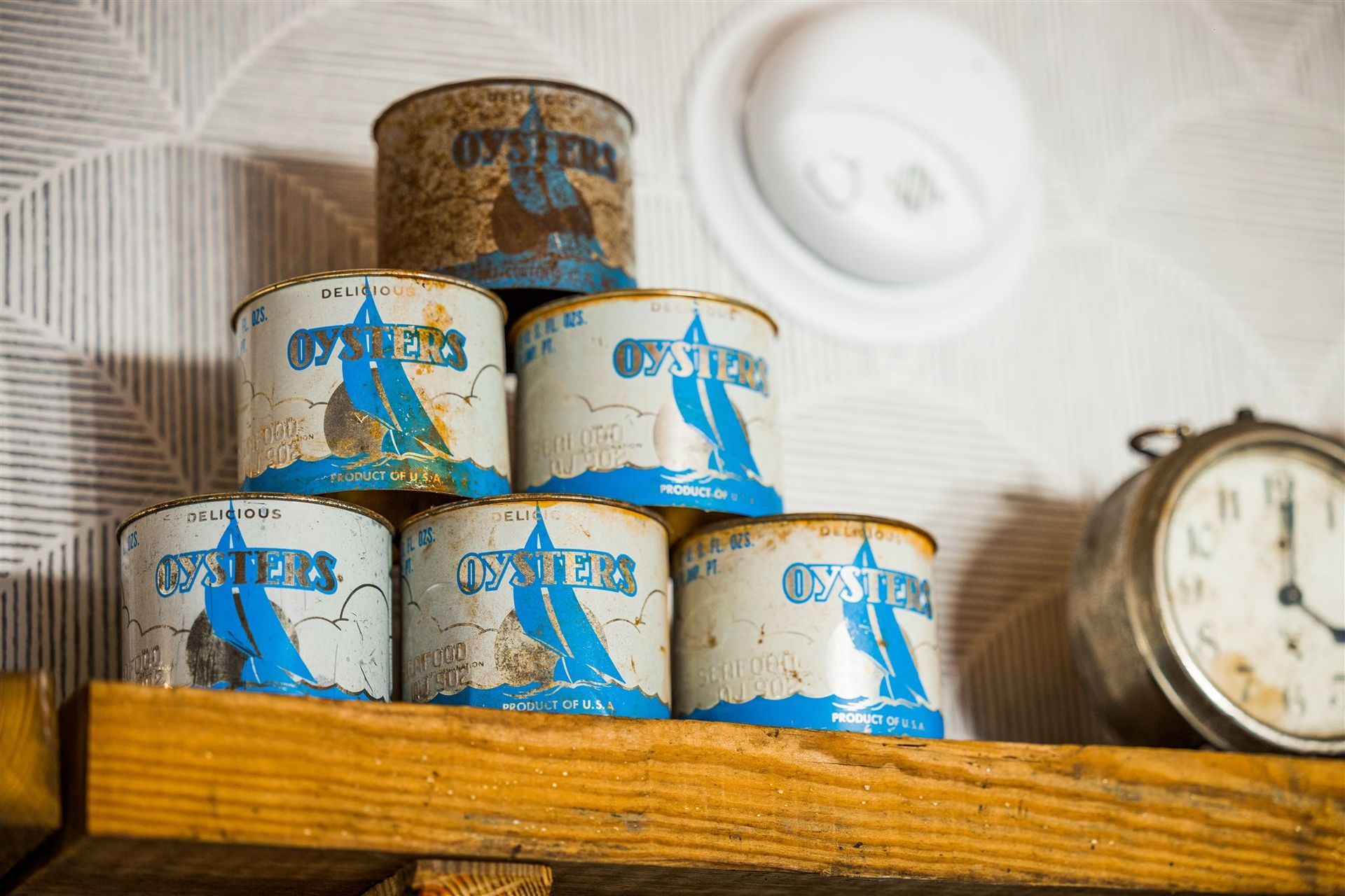 six cans of oysters are stacked on top of each other on a wooden shelf next to an alarm clock .