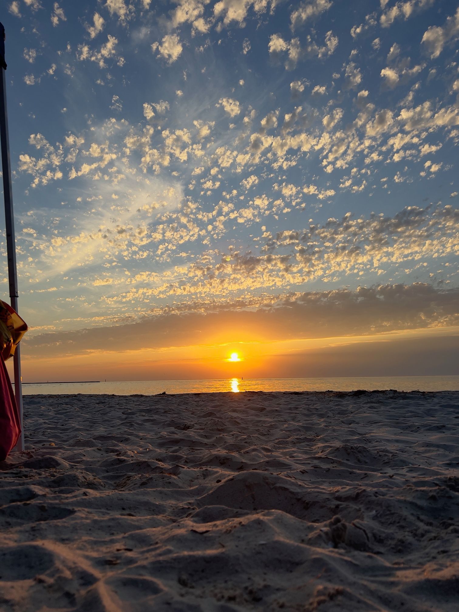 a person is standing on a beach watching the sun set over the ocean .