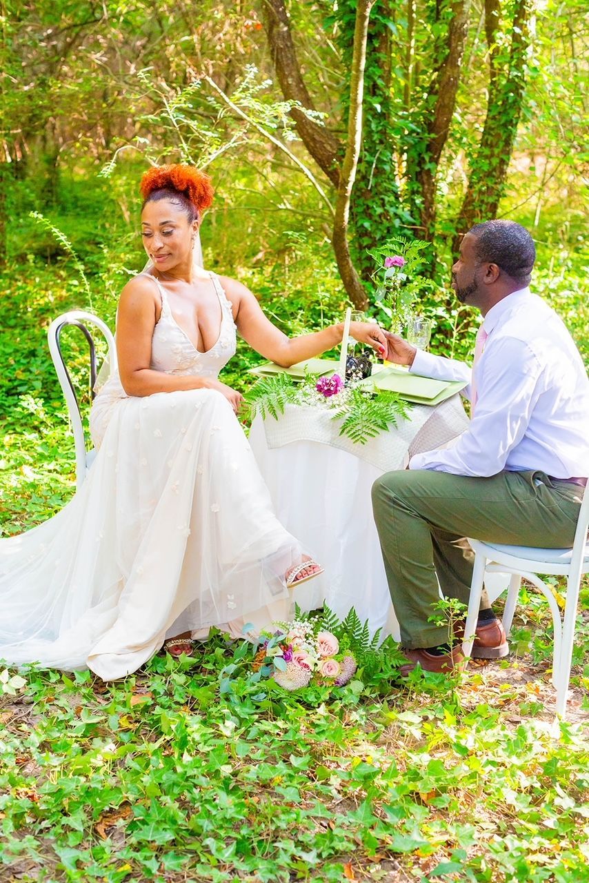 a bride and groom are sitting at a table in the woods .