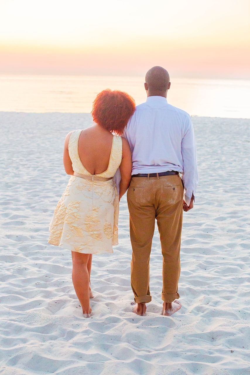 a man and a woman are standing on a beach looking at the ocean .