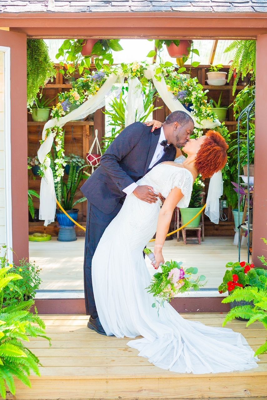 a bride and groom are kissing in front of a greenhouse .