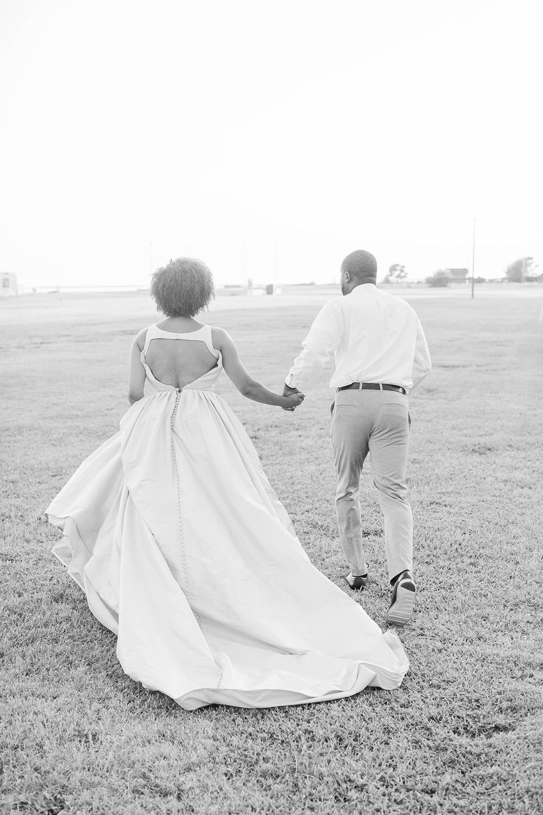 a bride and groom are holding hands and running through a field .