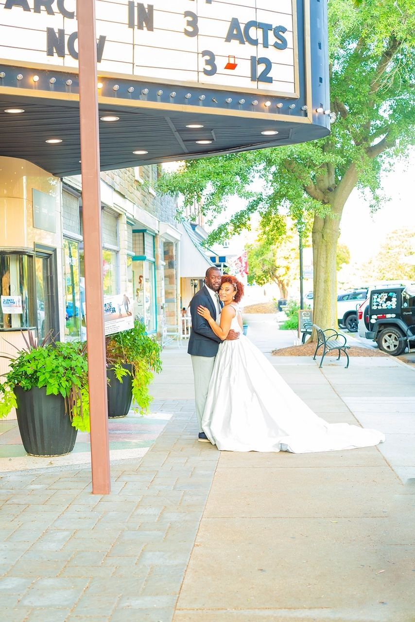 a bride and groom are posing for a picture in front of a movie theater .