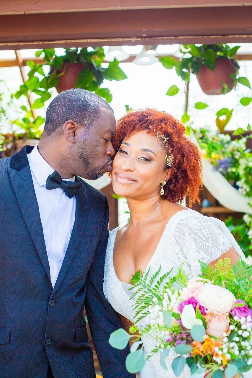 a man is kissing a woman on the forehead while holding a bouquet of flowers .