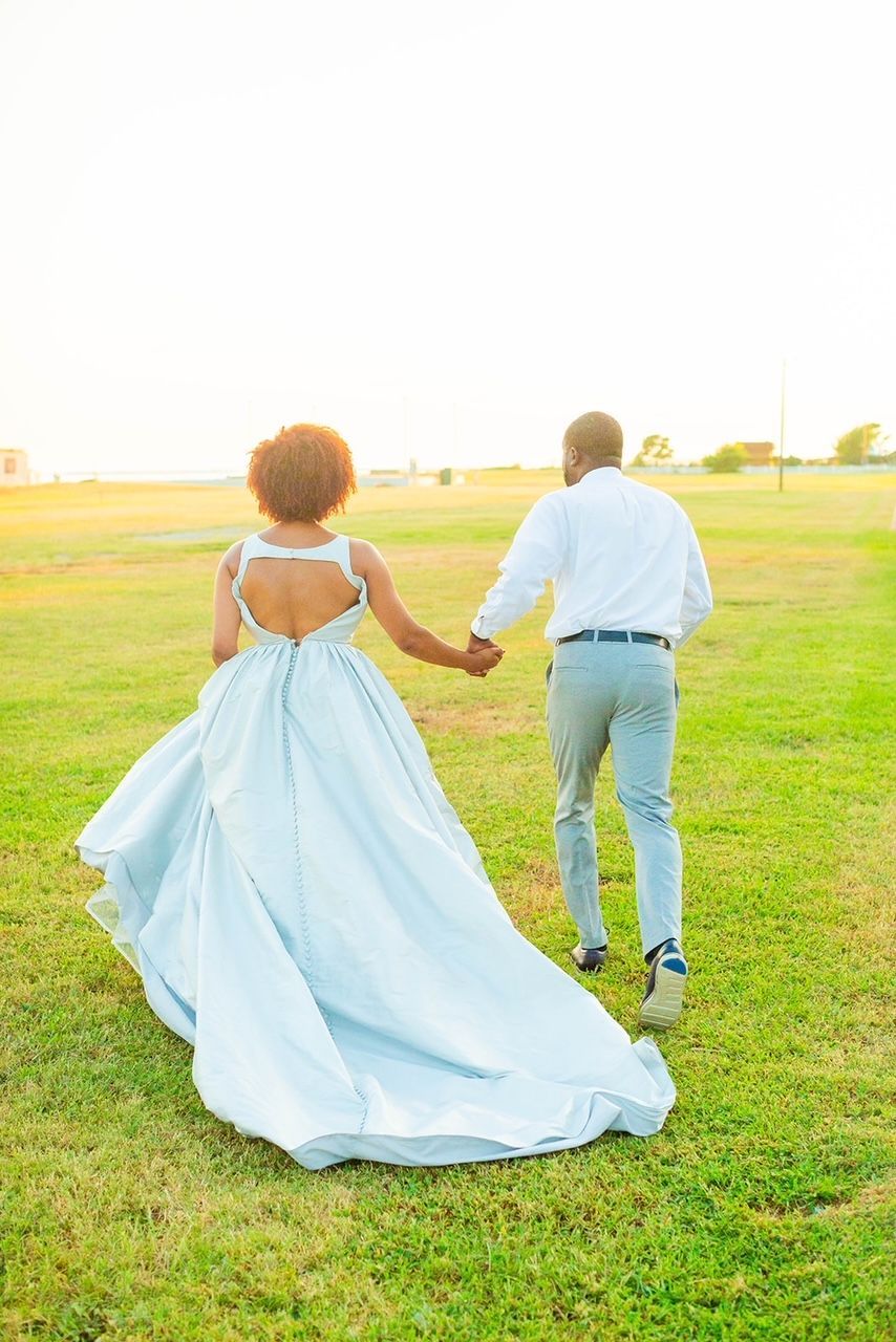 a bride and groom are walking through a grassy field holding hands .