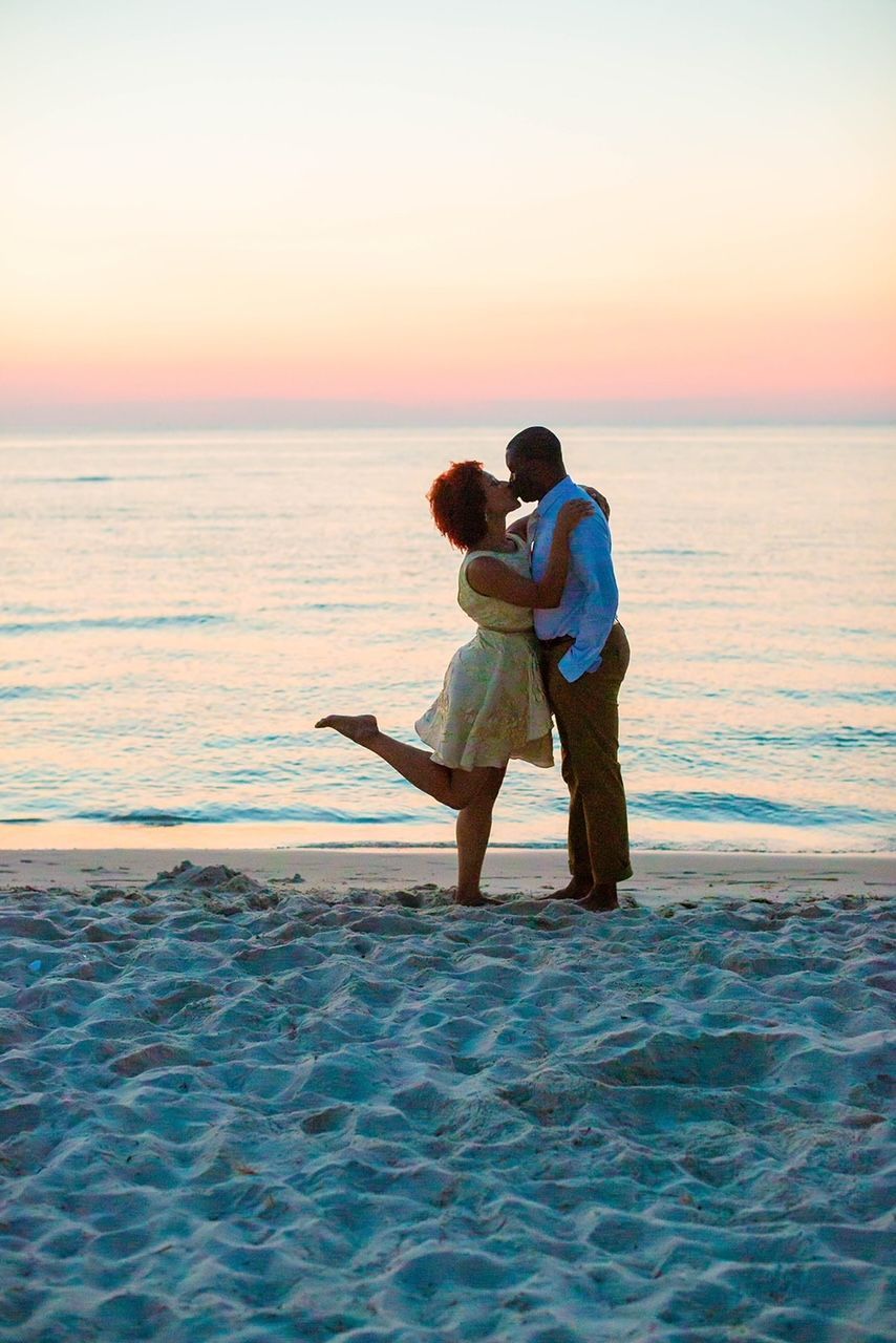 a man and woman are kissing on the beach at sunset .