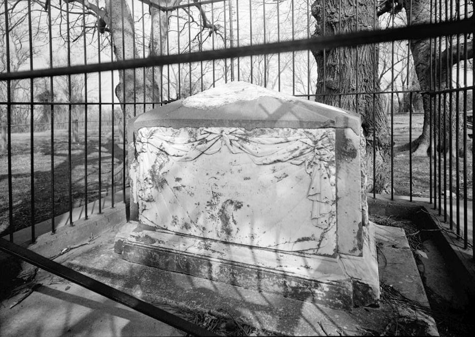 a black and white photo of a grave in a cemetery behind a fence .