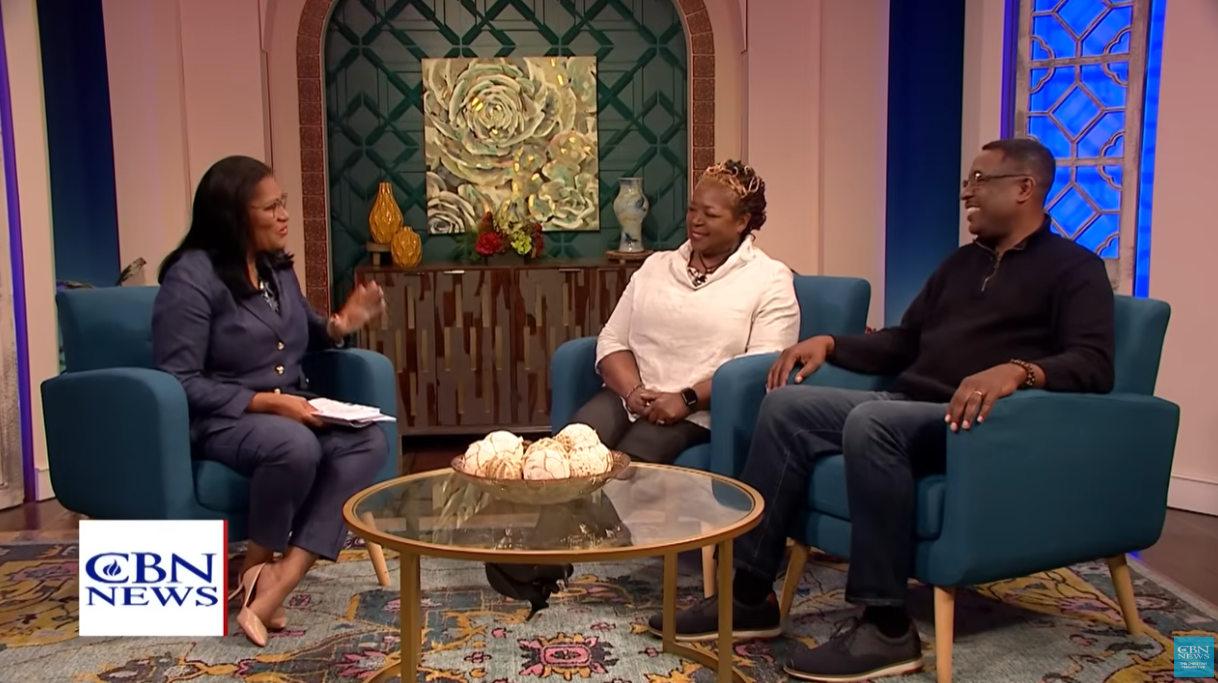 A man and a woman are sitting in chairs talking to a woman on a television show.