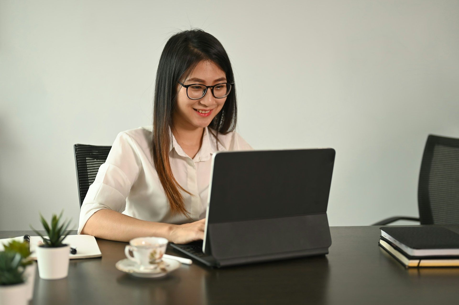Woman wearing glasses smiles while working on a tablet at a desk.