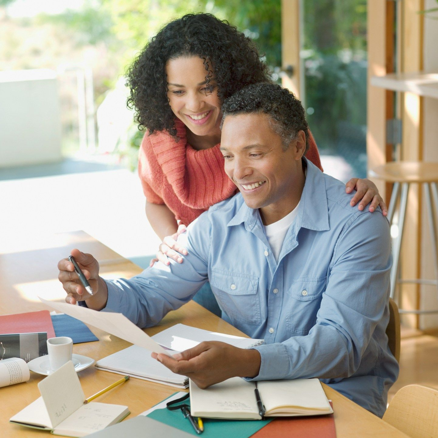 Couple reviews documents at a table. Woman smiles, placing a hand on the man's shoulder.