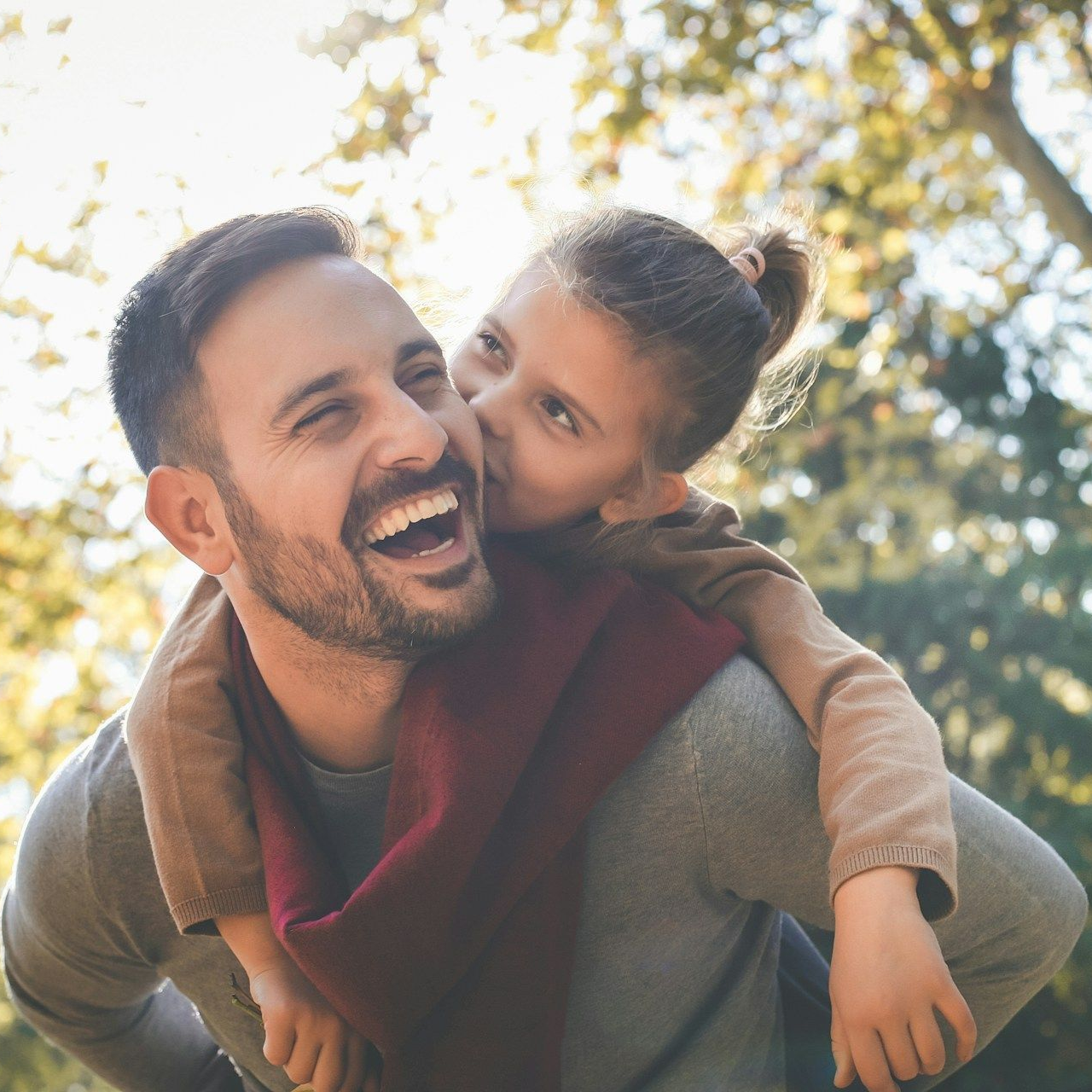 Man smiling while being kissed on the cheek by a child outdoors.