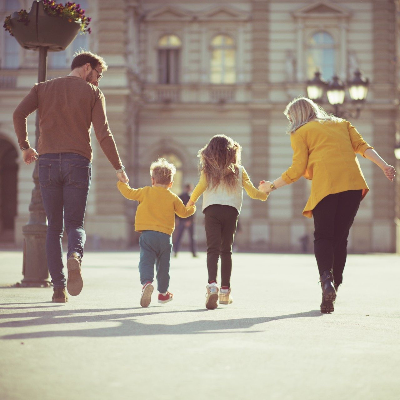 Family holding hands and walking in a city square, sunny day.