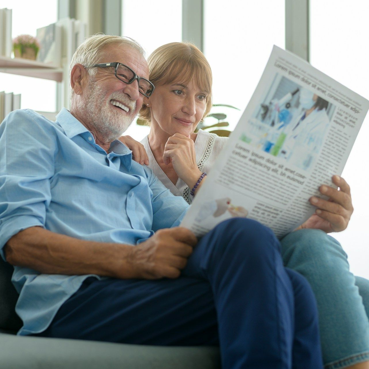 Smiling couple reading newspaper together on a couch.