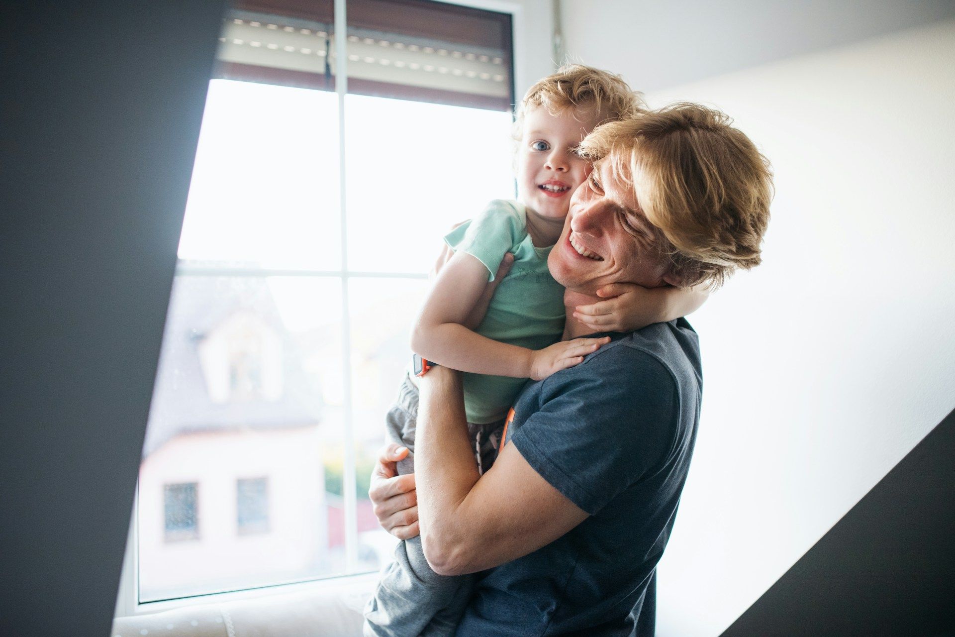 Person holding and smiling at a child near a window.