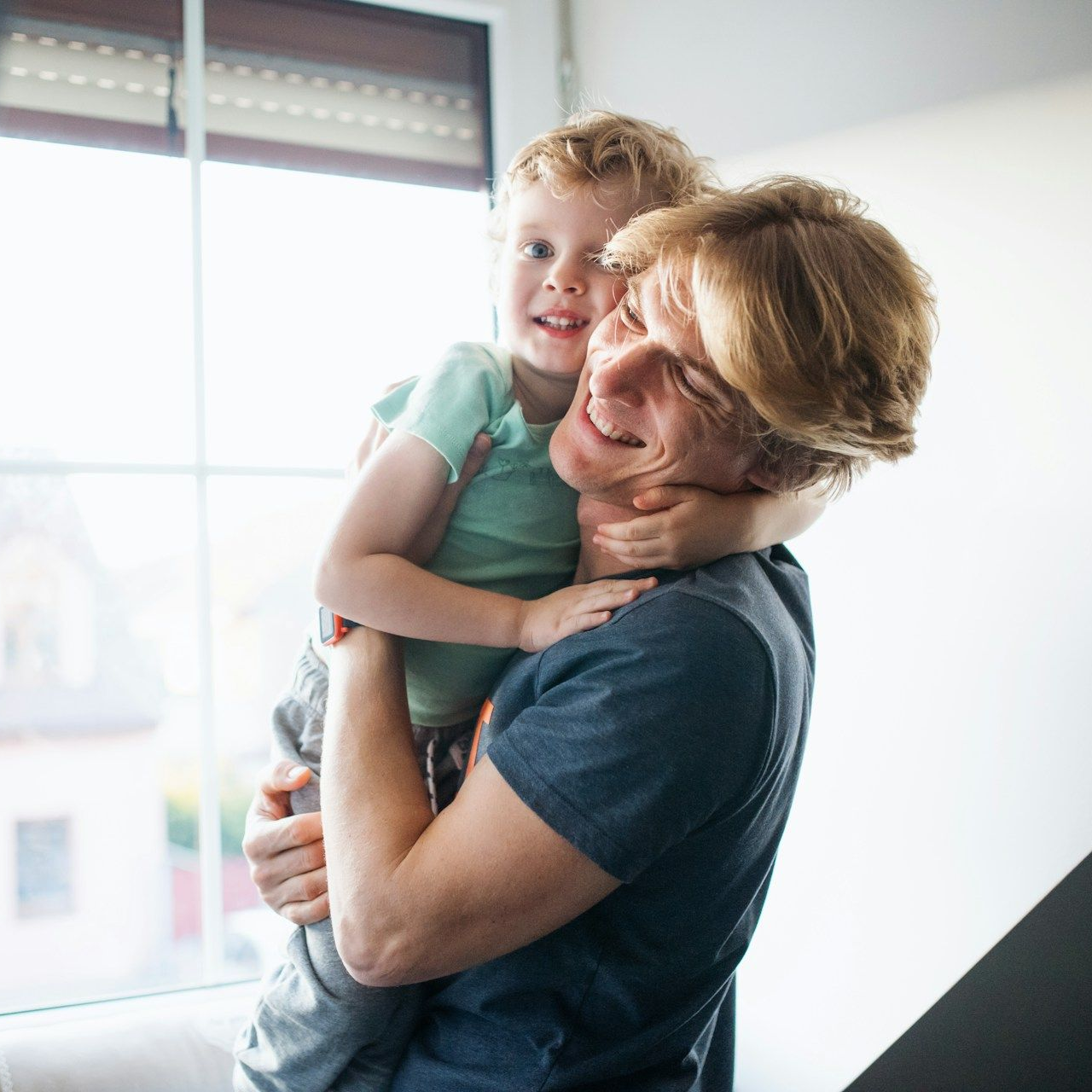 Man holding a young child near a window, both smiling.