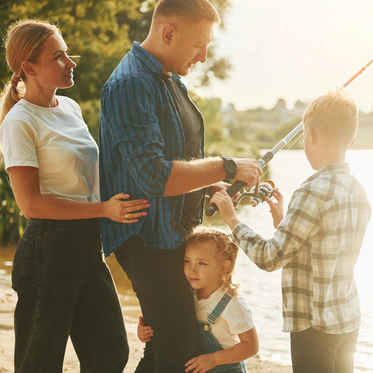 Family fishing at a lake; father holding rod, son and daughter watching, mother nearby.
