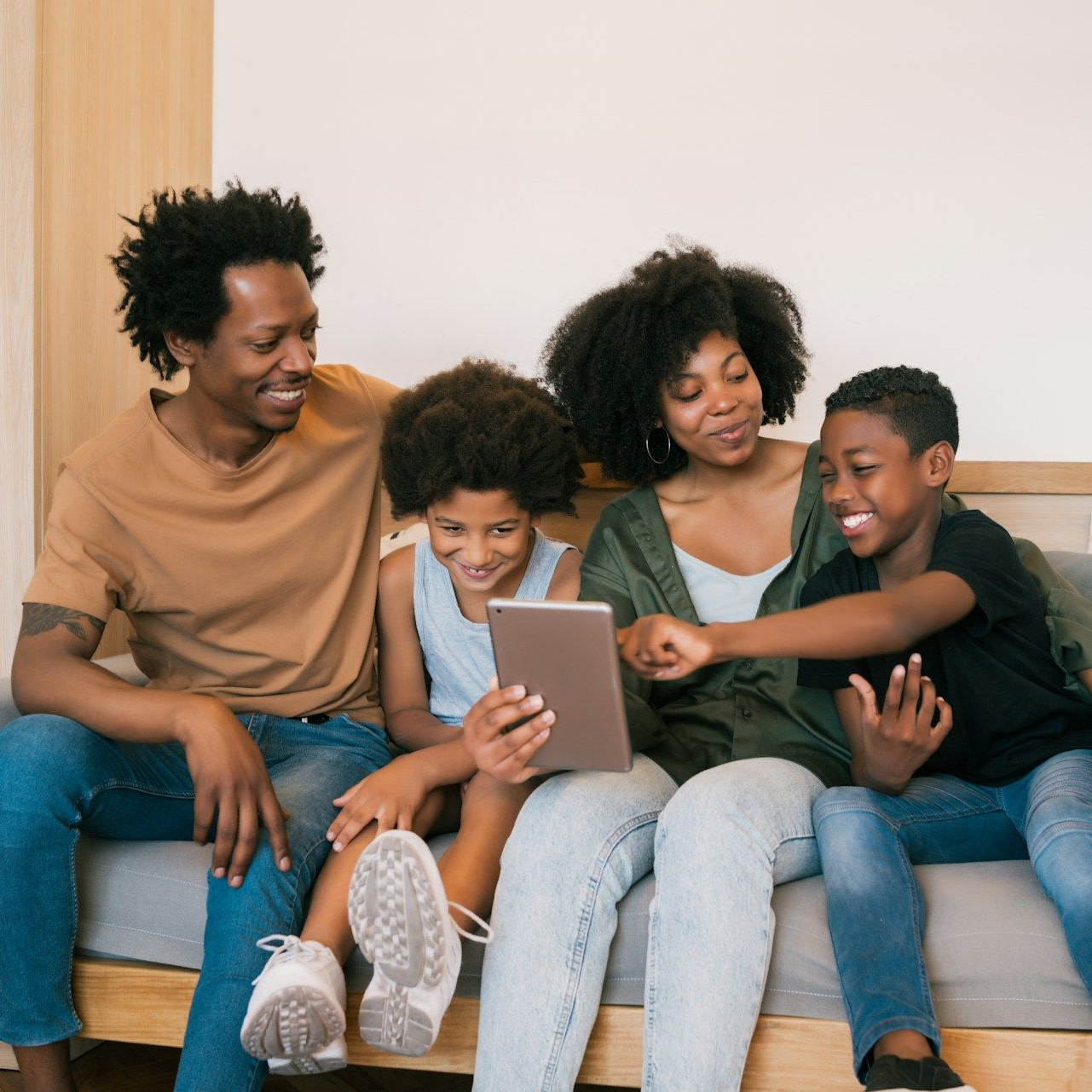 Family of four on a couch looking at a tablet, smiling.