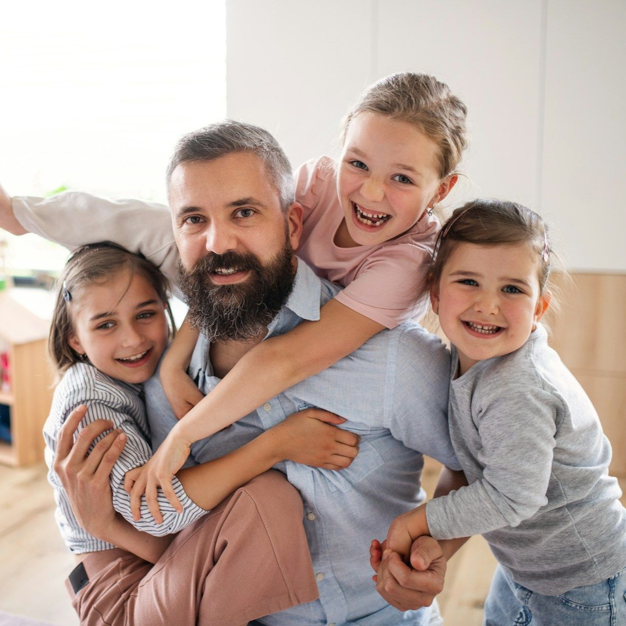 Man smiles, carrying three laughing children indoors.